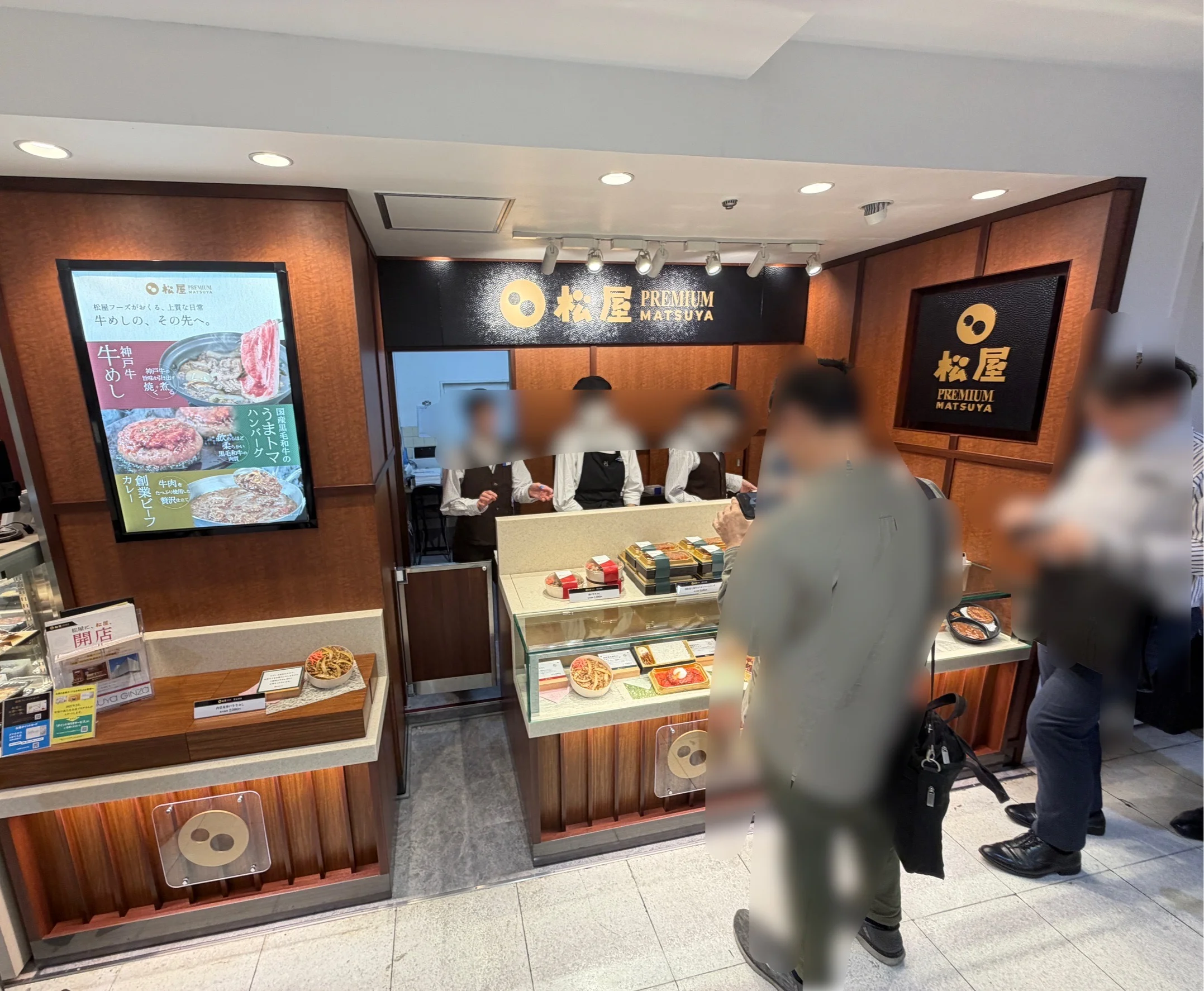松屋PREMIUM 銀座店の店頭外観。黒地に金色で『PREMIUM MATSUYA』のロゴ看板、左手にデジタル看板『牛肉の、その先へ。』、ガラスケース内に商品弁当、カウンターには販売員と客が並ぶ